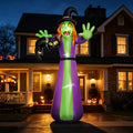 Giant green-faced witch inflatable in a purple robe holding a black cat in front of a house at night