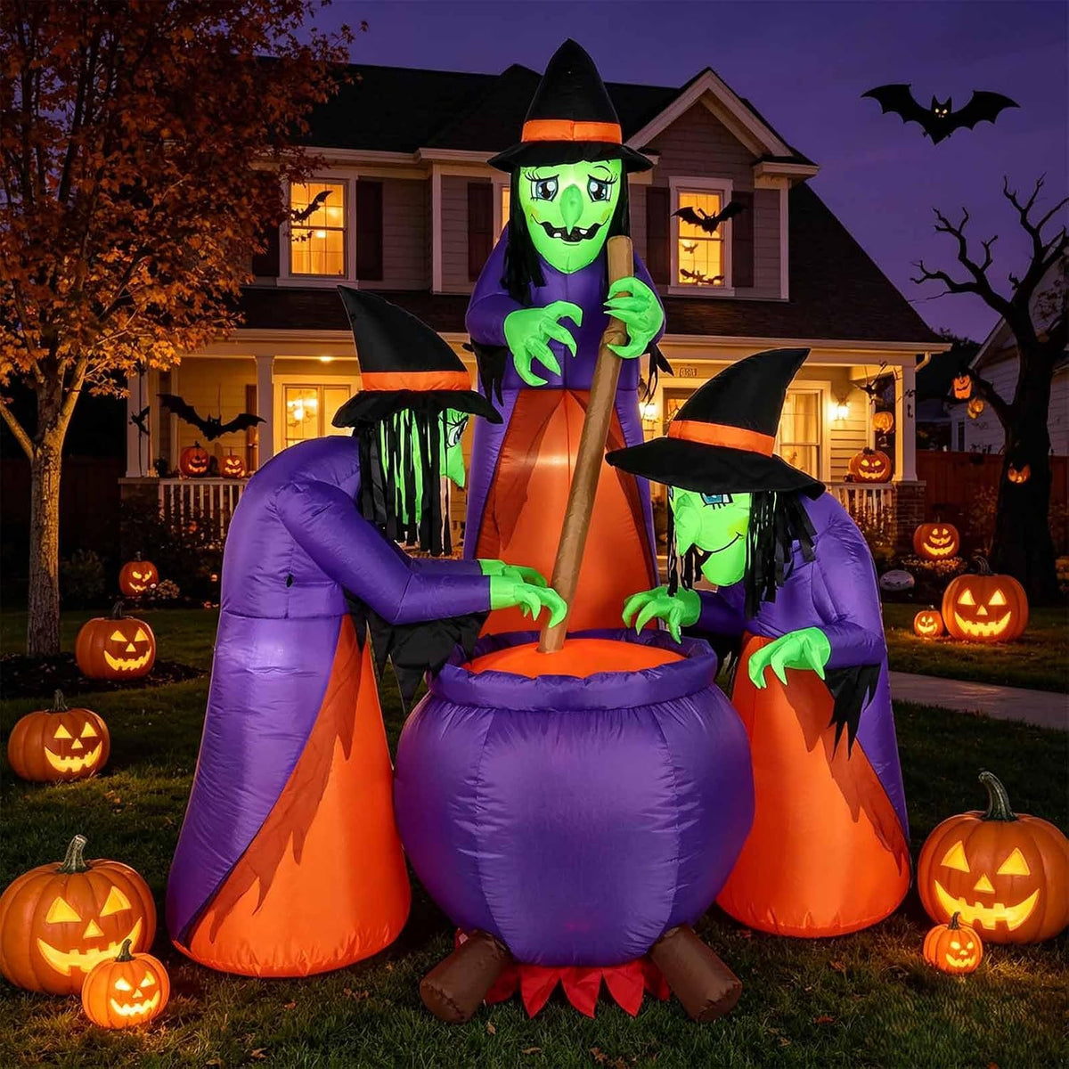 Three green-faced witches stirring a purple cauldron inflatable in a yard at dusk