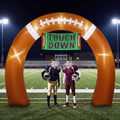 Brown football-shaped inflatable arch with a Touch Down banner on a lit football field with two players