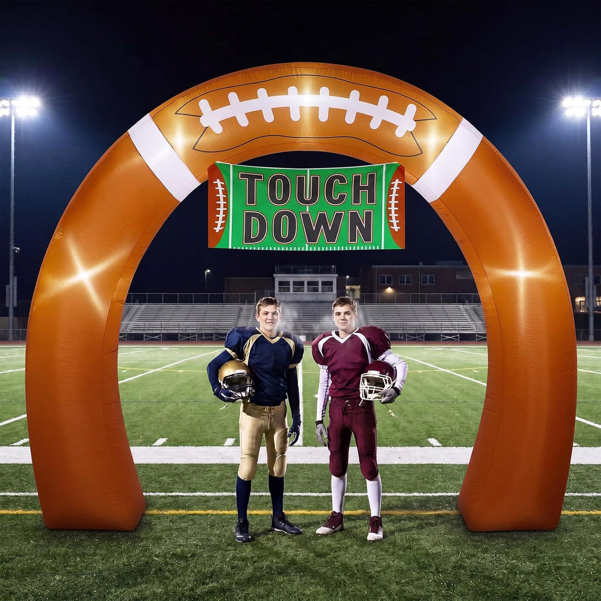 Brown football-shaped inflatable arch with a Touch Down banner on a lit football field with two players