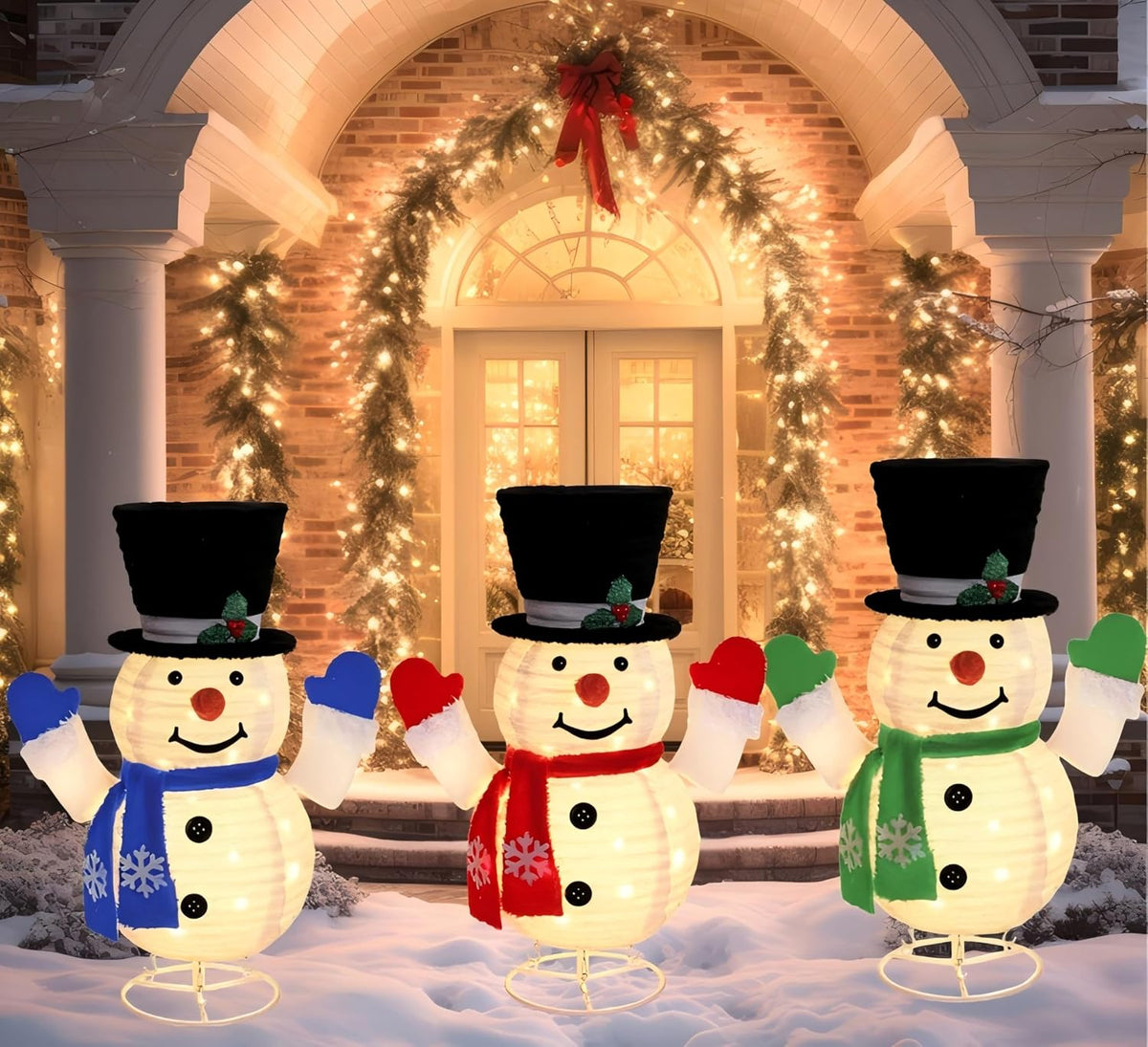 Three lighted pop-up snowmen in top hats with colored scarves in front of a decorated doorway