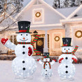 Three sparkling lighted snowmen in top hats of different heights in front of a snowy house