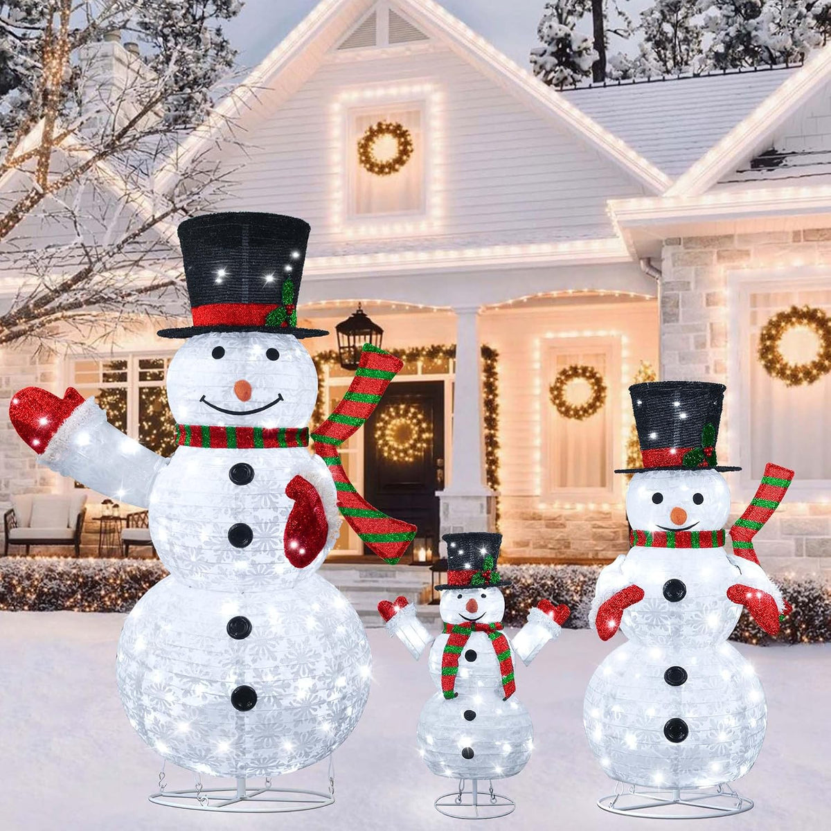 Three sparkling lighted snowmen in top hats of different heights in front of a snowy house