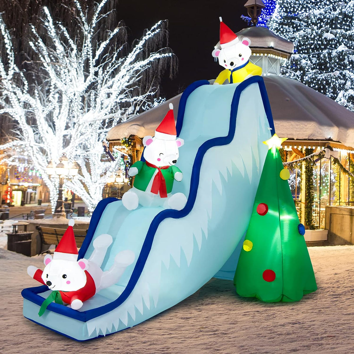 Polar bears in Santa hats sliding down a blue snow slide inflatable next to a small Christmas tree
