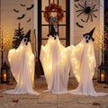 Three glowing white draped ghosts in black witch hats standing on a porch with bats on the wall