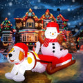 Snowman in a Santa hat on a red sleigh pulled by a white puppy inflatable in front of a lit house